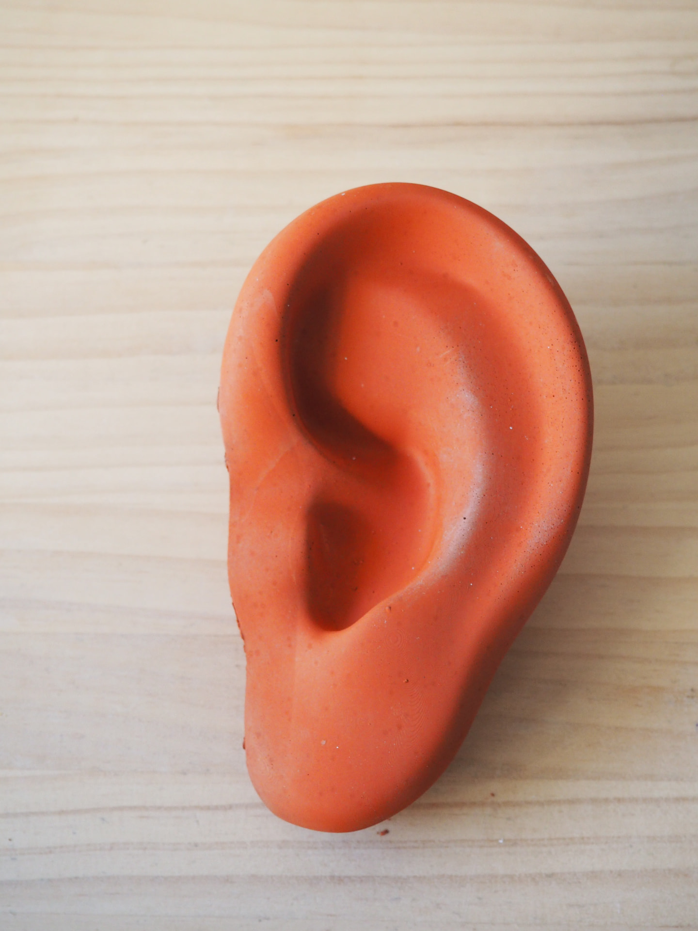 Colgador cerámico con forma de oreja en color naranja sobre madera clara, pieza de producto propio de Biburu